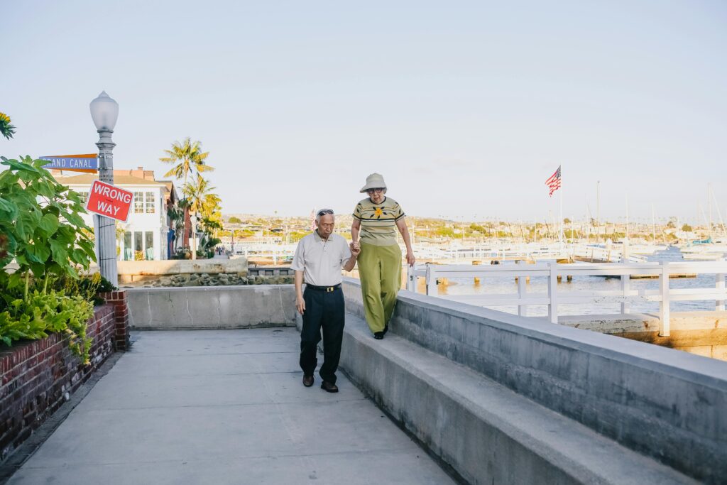 Una pareja de ancianos en su proceso de envejecimiento cogidos de la mano. Están andando al lado del mar. 