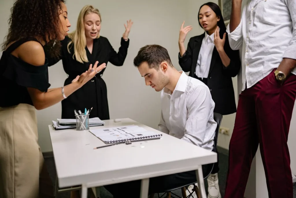 Grupo de personas mirando y señalando a un compañero de trabajo echándole la culpa por algún motivo desconocido. 